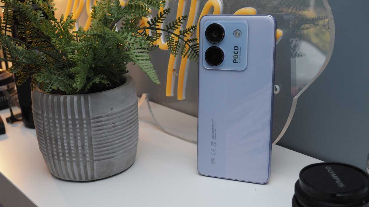 A photo of the Poco M7 Pro against a neutral backrground on a wooden shelf